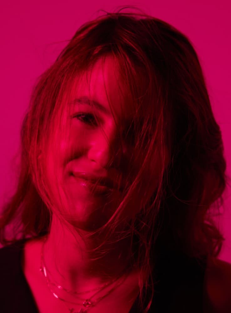 Ashley Nader photographed under a magenta gel, hair across her face, mid-laugh